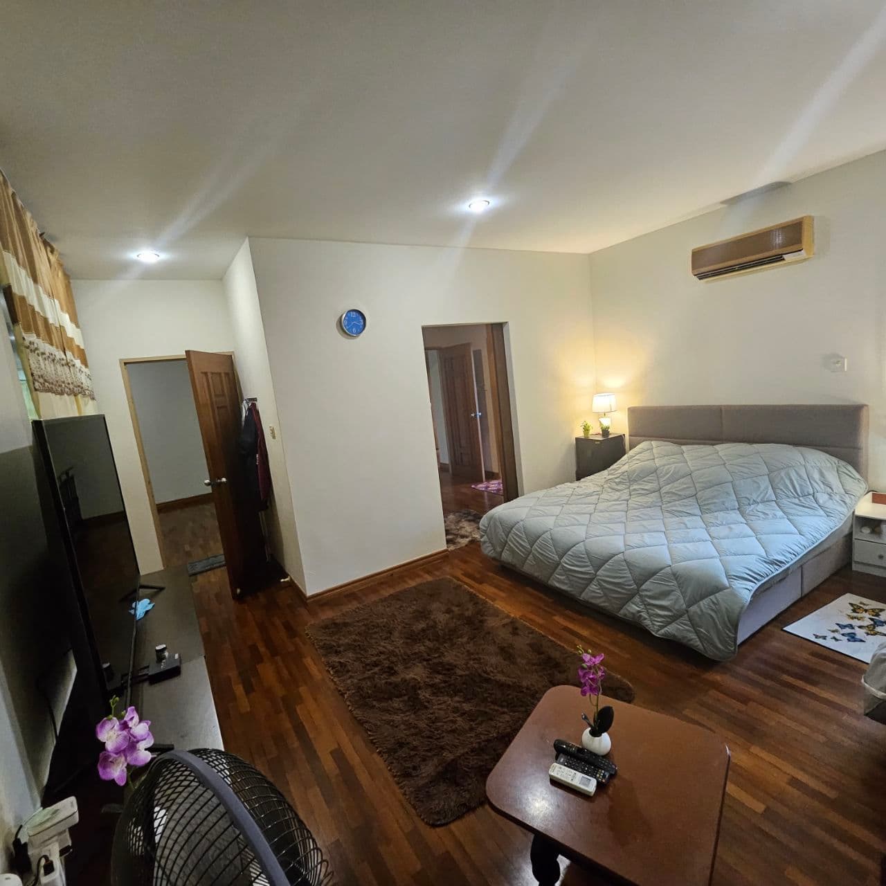 Bedroom with a quilted bed, dark wood floors, a brown rug, and a television.