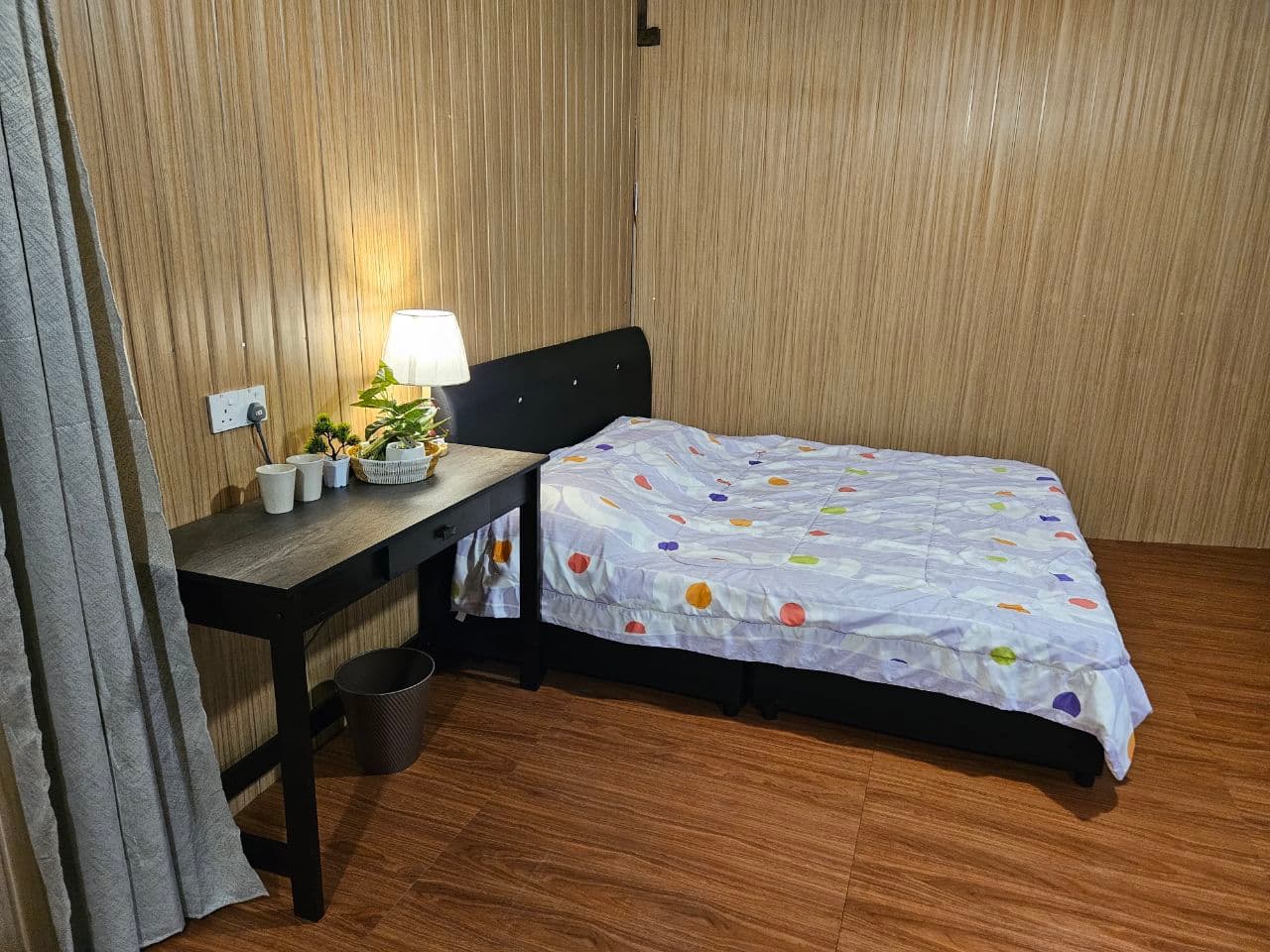 Wood-paneled bedroom with a single bed, patterned duvet, and a desk with a warm lamp.