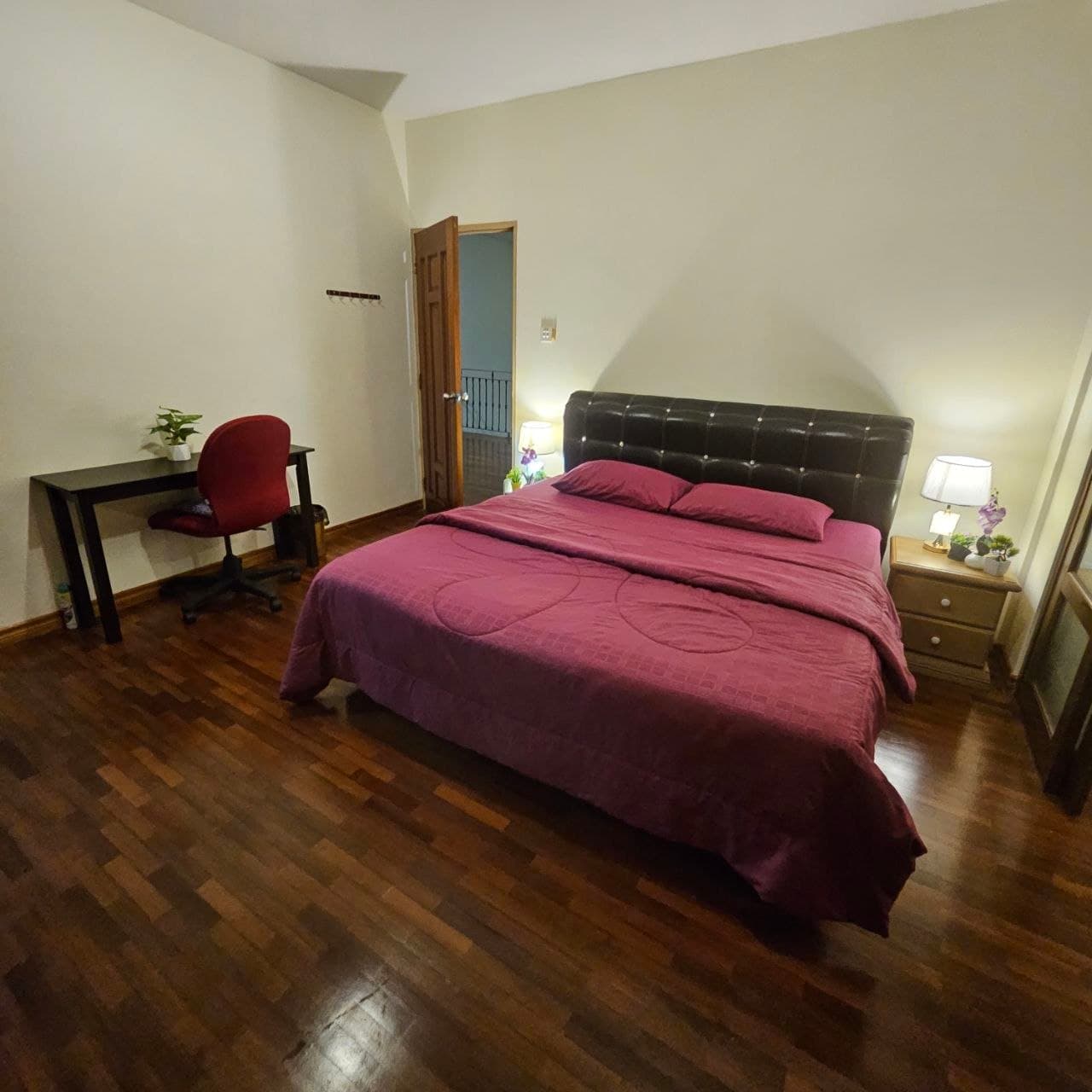 Bedroom with a maroon bed, dark wood floors, and a desk with a red office chair.