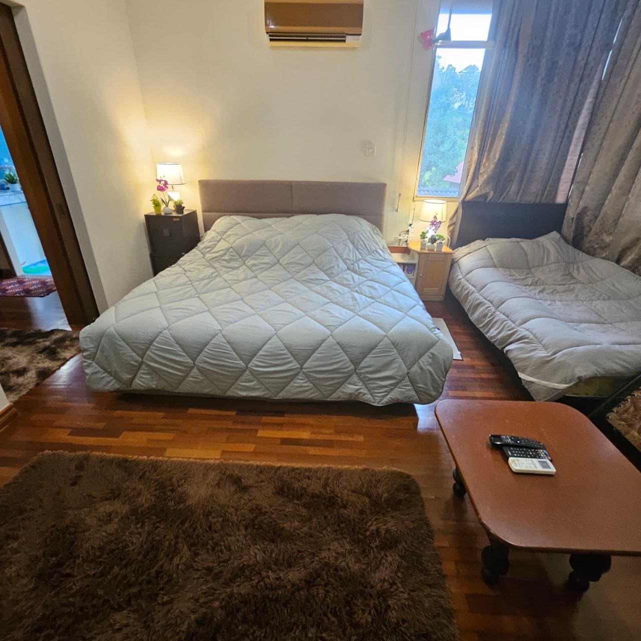 Bedroom with two beds, light blue quilted comforters, wooden floors, and a brown shaggy rug.