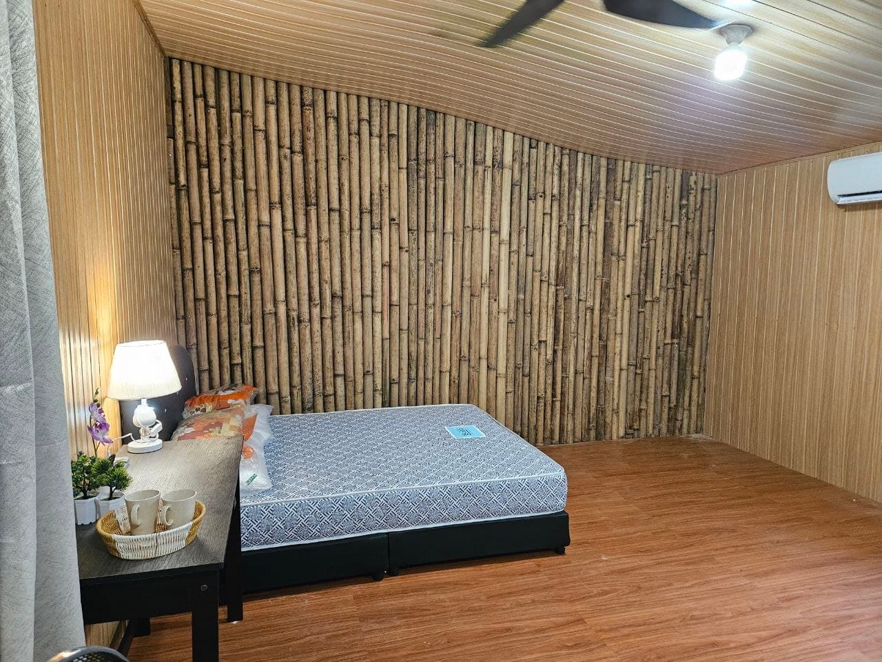 Cozy bedroom with a bamboo pole wall, patterned mattress, and warm wooden floors and ceiling.